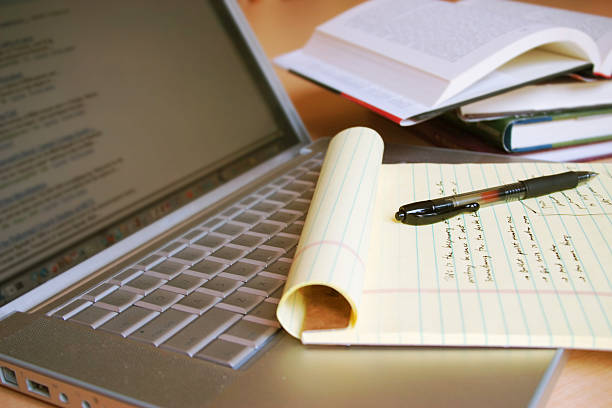 Notepad on a laptop that is next to open books all on a desk