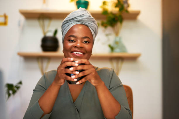 Portrait of African woman wearing turban on her head while sitting at her desk drinking coffee and looking cheerful